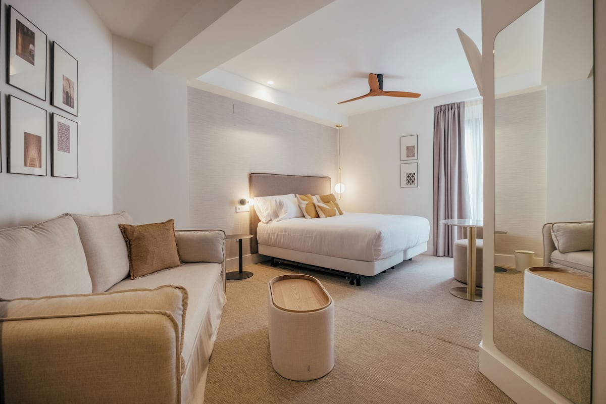 Une chambre d’hôtel moderne équipée d’un lit, d’un canapé, d’une lampe sur pied et d’un ventilateur de plafond.