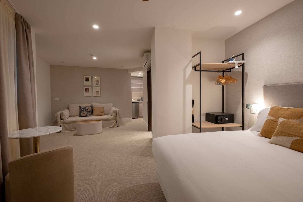 Une chambre d’hôtel avec un grand lit, un canapé, une petite table, une table de chevet, une étagère murale et une armoire.