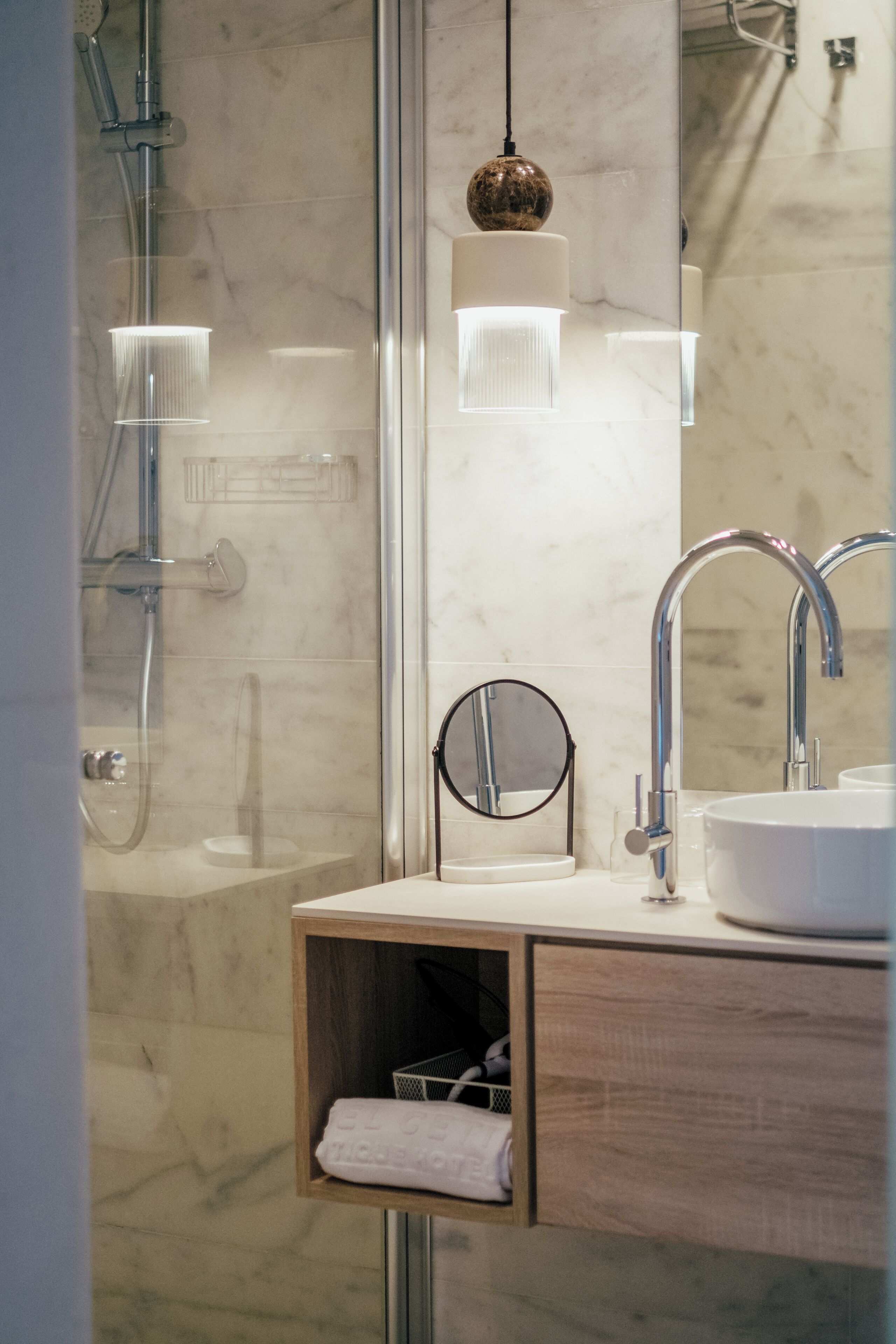 A modern bathroom with a glass-enclosed shower, a round mirror, and a wooden cabinet with a towel.