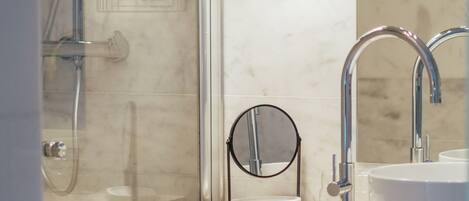Une salle de bain moderne avec une douche à parois de verre, un miroir rond et un meuble en bois contenant une serviette.