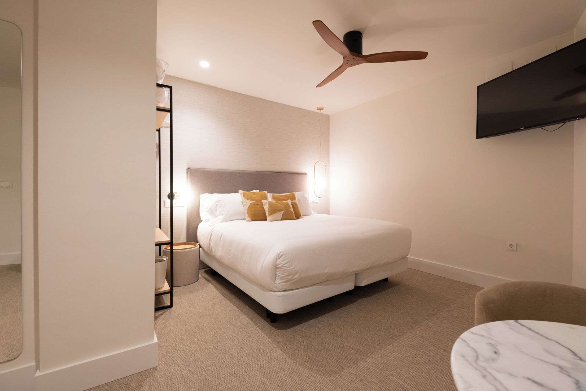 Una habitación de hotel moderna con una cama grande, un ventilador de techo, un televisor de pantalla plana y una pequeña mesa.