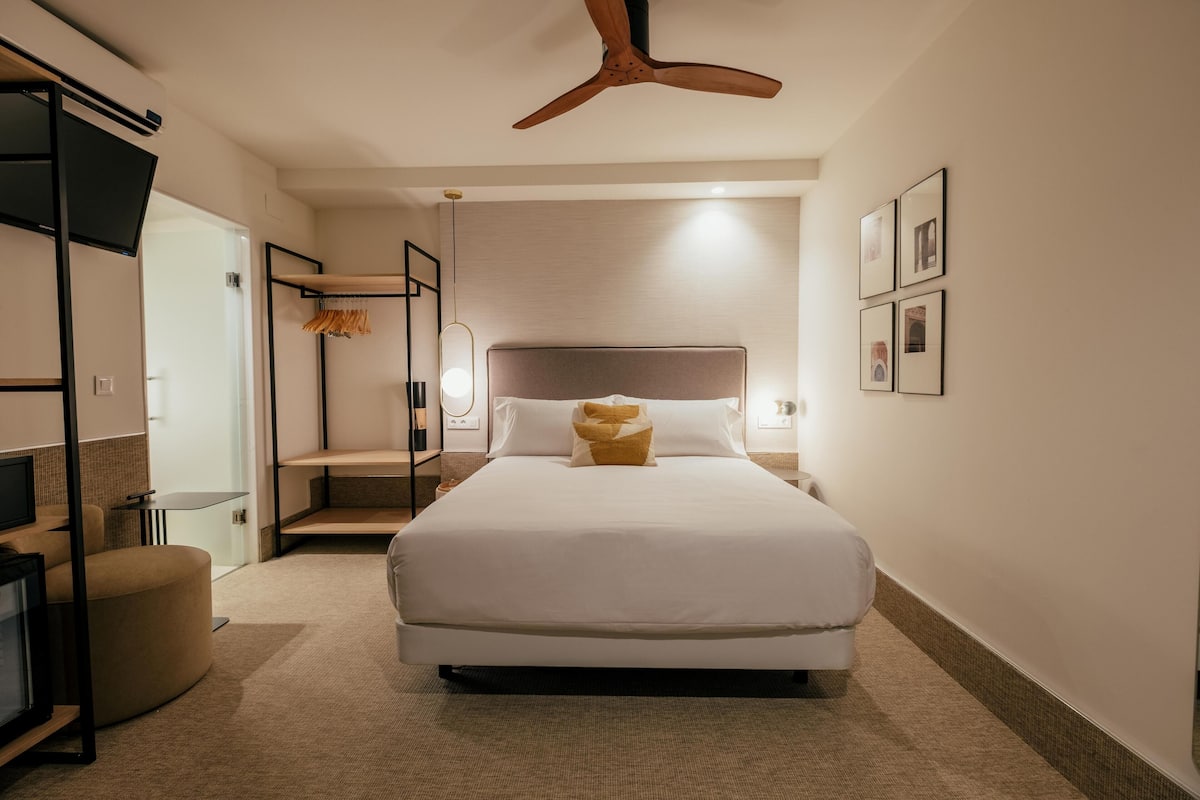 Une chambre d’hôtel moderne dotée d’un grand lit, d’un ventilateur de plafond, d’une télévision et d’un coin salon.