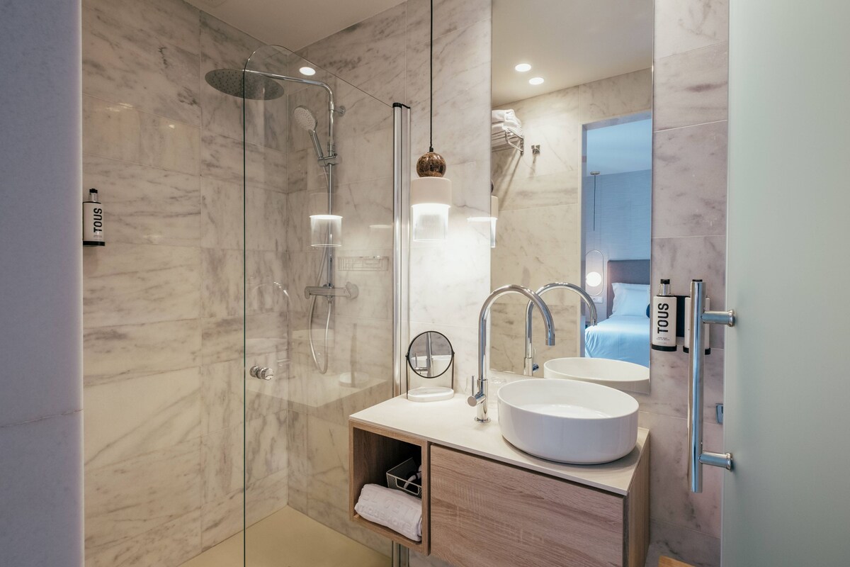 A modern bathroom with a glass-enclosed shower, a large mirror, and a white sink.