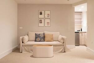 Ein Wohnzimmer mit einem beigen Sofa, einem runden Couchtisch und einer Wand mit gerahmten Bildern.