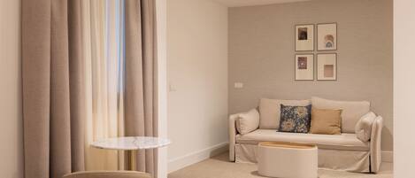 A modern hotel room with a beige sofa, a small round table, and a white ottoman.