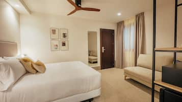 Une chambre d’hôtel avec un lit, un canapé, un ventilateur de plafond et des tableaux encadrés accrochés au mur.