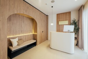 En moderne hotellobby med en træreception, et siddeområde med en bænk og et skilt monteret på væggen.