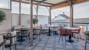 A covered outdoor seating area with tables and chairs, a tiled floor, and a view of buildings in the background. - Hotel Cetina Casa de Aguilar (Córdoba)