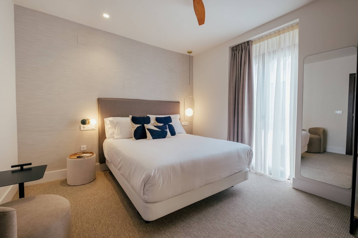 Une chambre d’hôtel moderne avec un grand lit, des tables de chevet, un bureau, un miroir et un ventilateur de plafond.