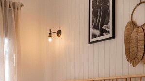 Una camera da letto con una testiera in legno, biancheria da letto bianca, una lampada sul comodino, un quadro appeso alla parete e un cesto di vimini a sospensione.