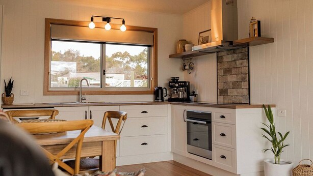 Una cucina moderna con mobili bianchi, un'ampia finestra e un'area pranzo con tavolo e sedie in legno.