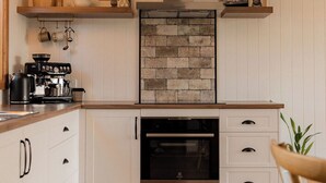Una cucina moderna con mobili bianchi, forno a incasso, zoccolo in pietra e ripiani in legno.