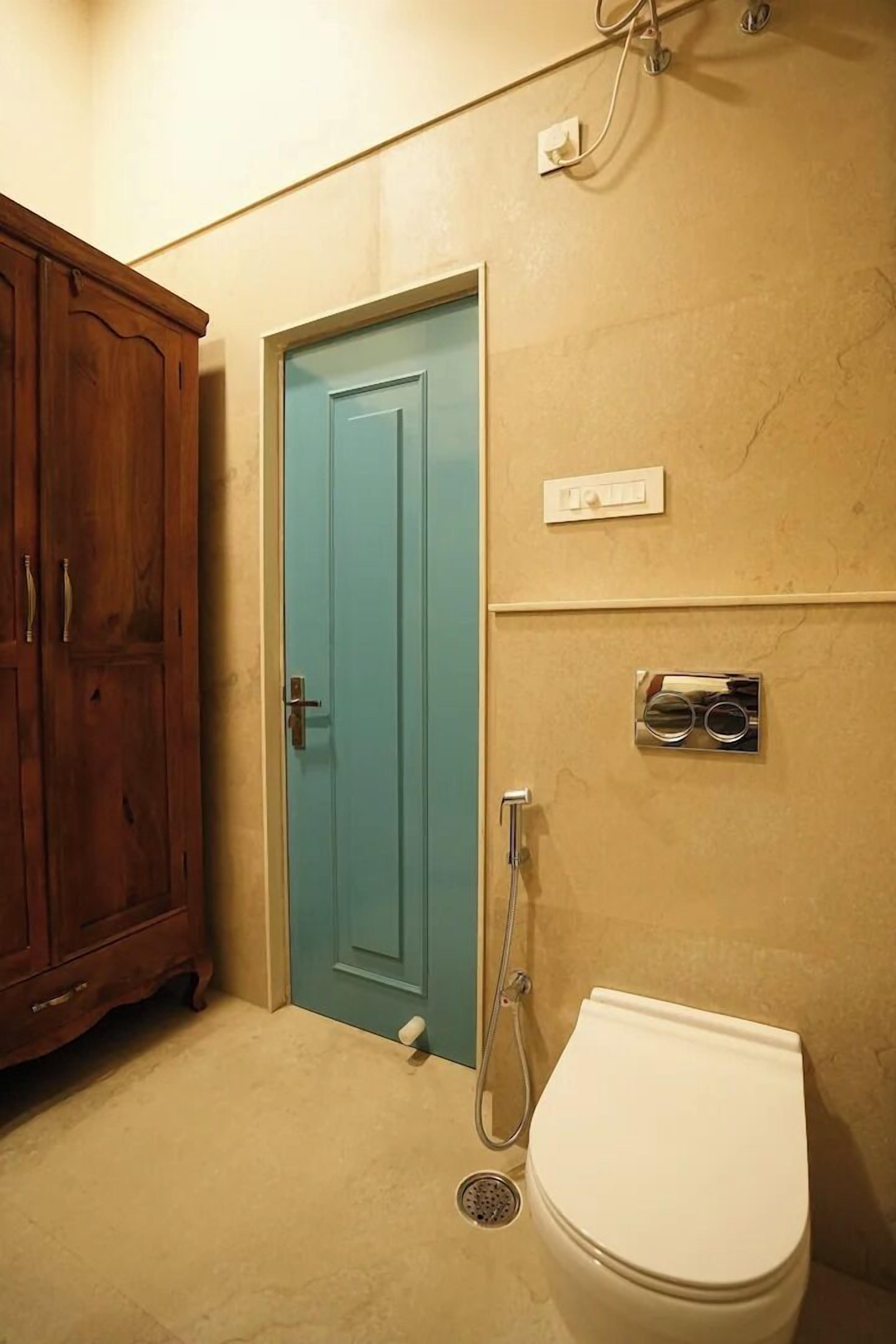 A bathroom with a wooden cabinet, a turquoise door, a white toilet, and a shower.