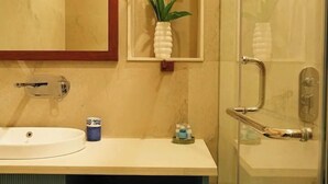 Un bagno con un lavandino bianco, uno specchio, una cabina doccia in vetro e un vaso con fiori gialli.