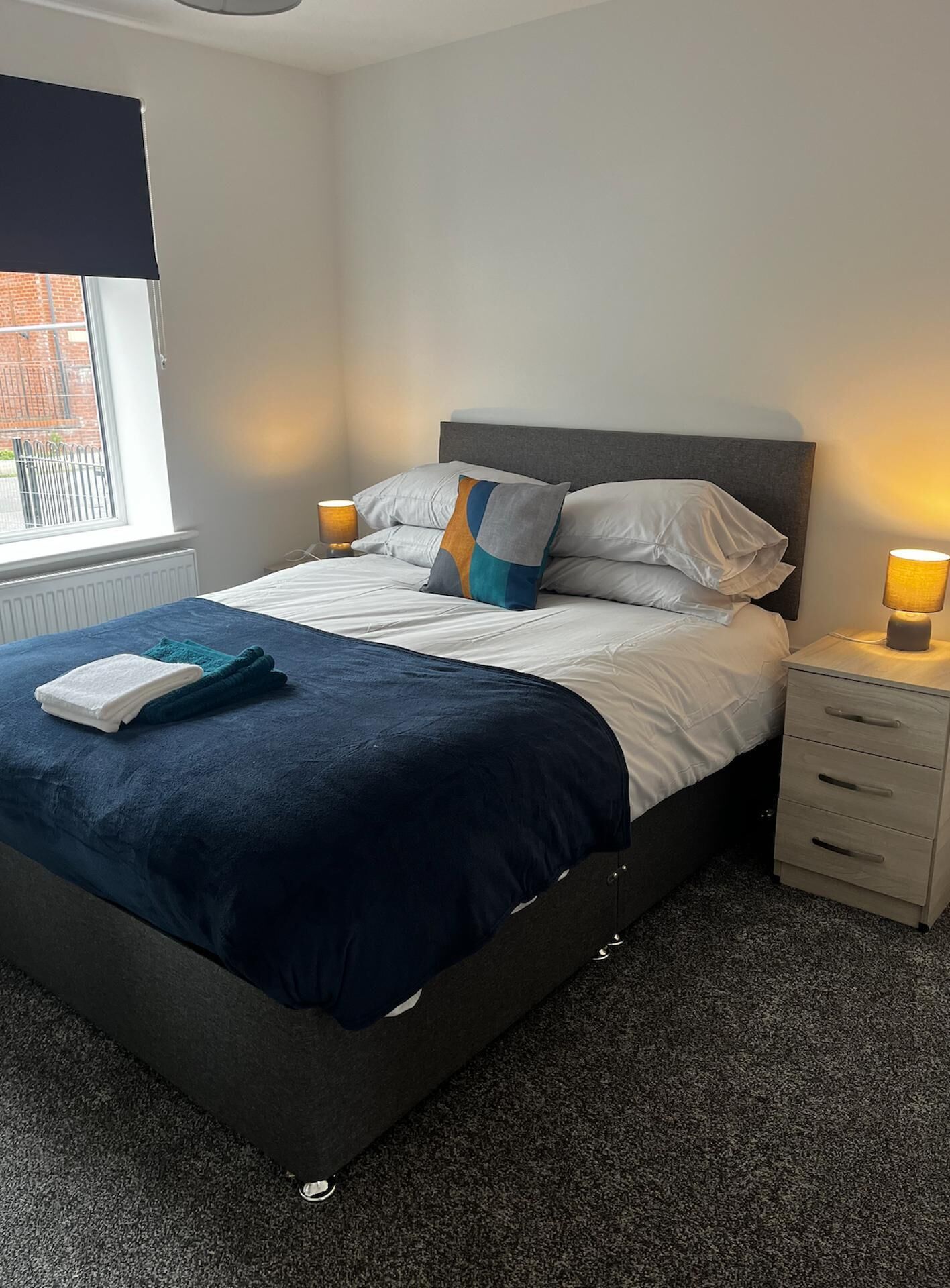 Een slaapkamer met een bed, nachtlampen, een raam en een radiator.