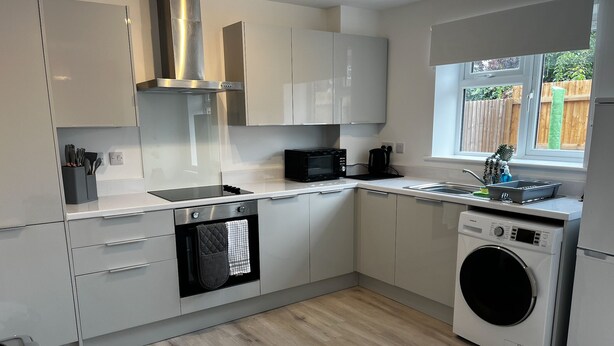 A modern kitchen with white cabinets, a built-in microwave, a washing machine, and a window overlooking a garden. - 2 Bed Flat - Sleeps 4 - Pets - Garden - Parking (Nottingham)