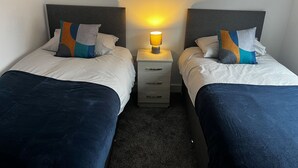 A double room with two beds, each with a headboard, a bedside table with a lamp, and a carpeted floor. - 2 Bed Flat - Sleeps 4 - Pets - Garden - Parking (Nottingham)