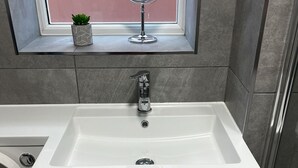 Ein Badezimmer mit einem weißen Waschbecken, einem Spiegel darüber und einem kleinen Topfpflanzen auf der Fensterbank.