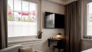 A hotel room with a bed, a desk with a chair, a TV mounted on the wall, and a window with curtains. - Frans&Frans hotel and apartments (Rauma)
