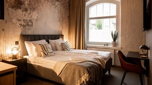 A bedroom with a large bed, a desk, a chair, a window with curtains, and a plant. - Frans&Frans hotel and apartments (Rauma)