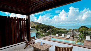 A modern outdoor pool area with a wooden deck, lounge chairs, and a table. - Luxury Penthouse with Private Jacuzzi and Pool in Saint-Martin (Saint-Martin)