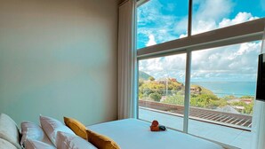 A bedroom with a large window, a bed with white and yellow pillows, and a view of a coastal area with buildings and a train track. - Luxury Penthouse with Private Jacuzzi and Pool in Saint-Martin (Saint-Martin)