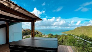 A balcony with a hot tub, wooden deck, and a view of the ocean and hills. - Luxury Penthouse with Private Jacuzzi and Pool in Saint-Martin (Saint-Martin)