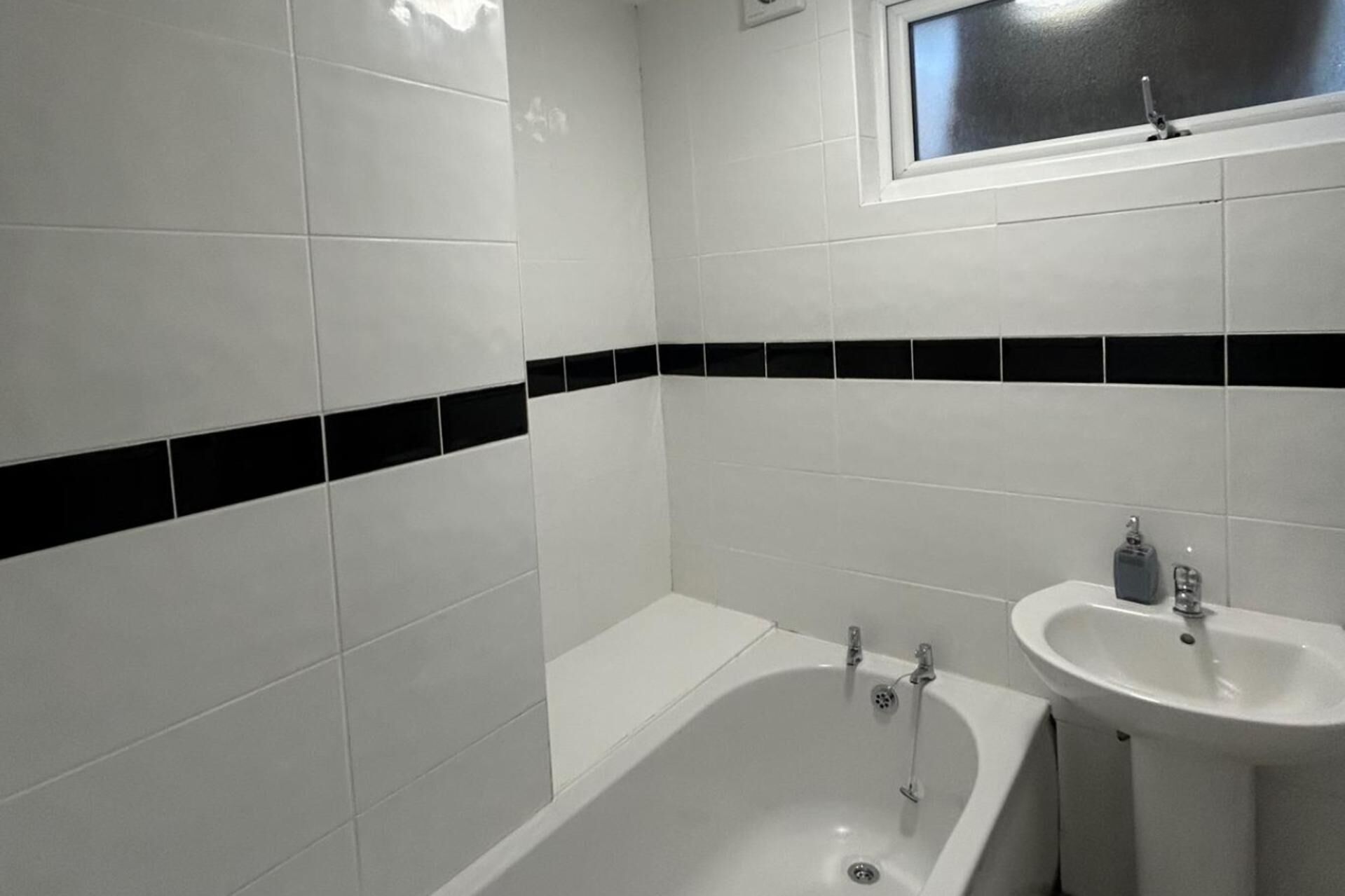 A bathroom with white tiles, a black horizontal stripe, a bathtub, and a sink.