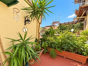 A balcony with potted plants, a wall-mounted light fixture, and a view of neighboring buildings. - Terrace Charming 3-bedroom apartment with WiFi, AC in Campo dei Fiori in Rome (Roma)