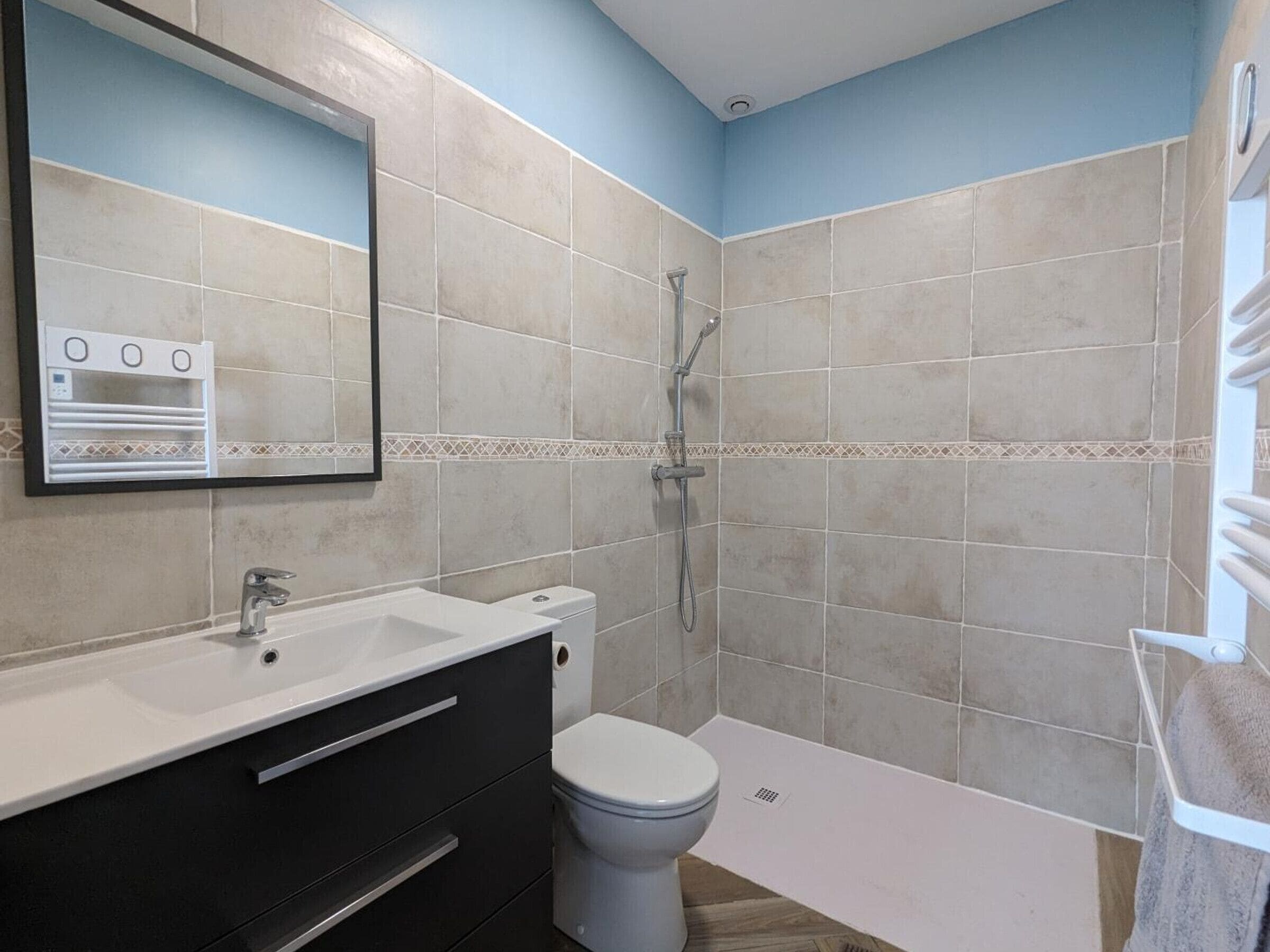 Un baño con lavamanos blanco, tocador negro y váter blanco.