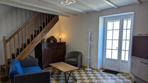 Ein Wohnzimmer mit Schachbrettmuster-Boden, einer Holztreppe, einem grauen Sessel, einem Holztisch, einem Kleiderständer und einem Fernseher.