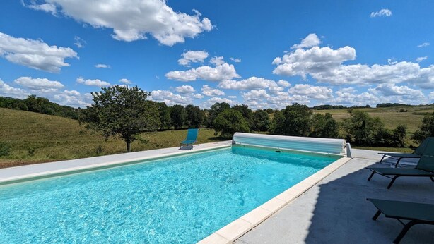 Ein rechteckiger Swimmingpool mit klarem, blauem Wasser, umgeben von einer Betonplattform. Auf einer Seite befinden sich Liegestühle und ein überdachter Bereich.