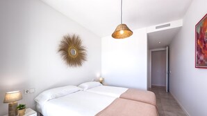 A modern bedroom with a large bed, bedside lamps, a decorative mirror, and a painting on the wall. - Modern apartment with terrace, pool, and Wi-Fi in Estepona (Estepona)