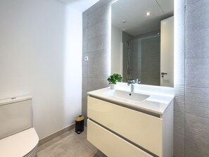 A modern bathroom with a toilet, a sink with a mirror, and a shower area. - Modern apartment with terrace, pool, and Wi-Fi in Estepona (Estepona)