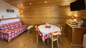 A cozy room with a wooden ceiling, a round table with a red tablecloth, a red and white patterned sofa, and a television mounted on the wall. - Spacious 2-room apartment for 5 people in Chinaillon (Le Grand-Bornand)