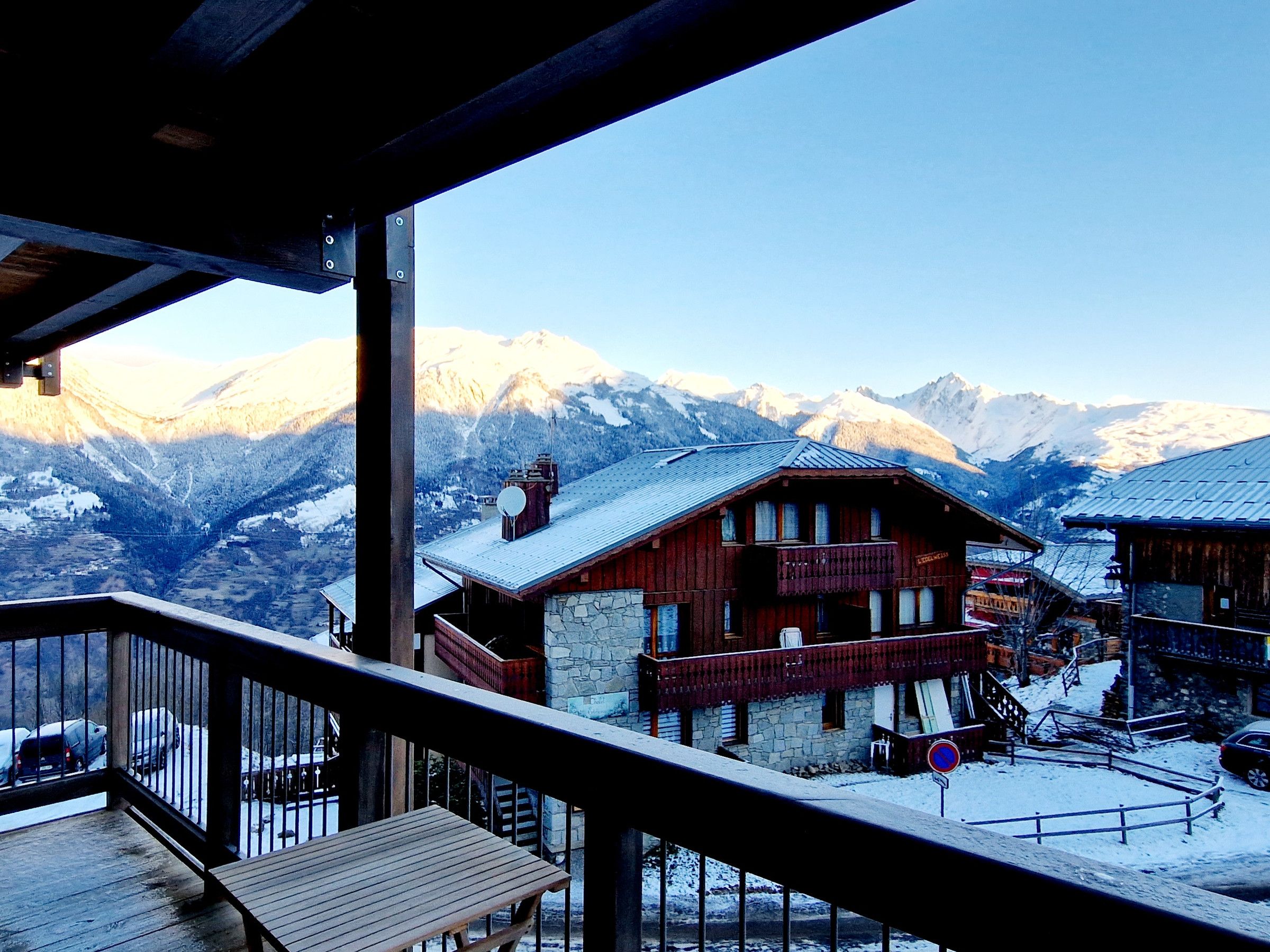 A wooden chalet with a stone foundation, a balcony, and a view of snow-covered mountains.