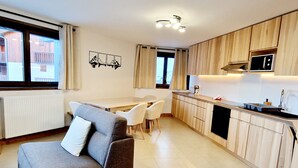 Una cocina moderna con armarios de madera, microondas integrado y un comedor con sofá gris y sillas blancas.