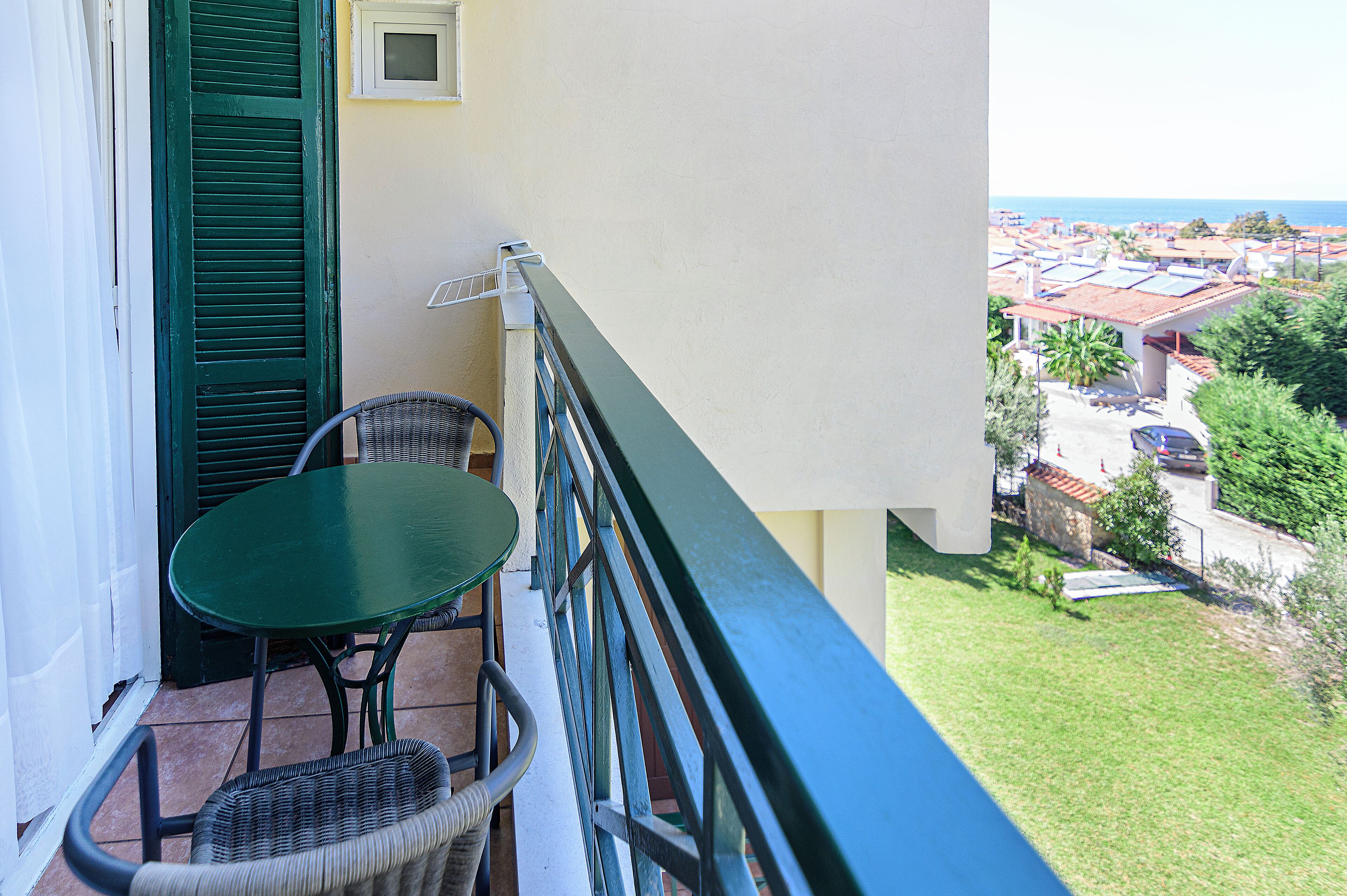 A balcony with a table and chairs, overlooking a residential area with houses and a view of the sea.
