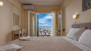 A hotel room with a large bed, a desk, a chair, a small table with a vase of flowers, and a balcony with a view. - Julia Hotel (Kassandra)