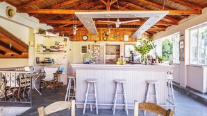 A rustic kitchen with wooden beams, a bar area with stools, and a stone floor. - Julia Hotel (Kassandra)