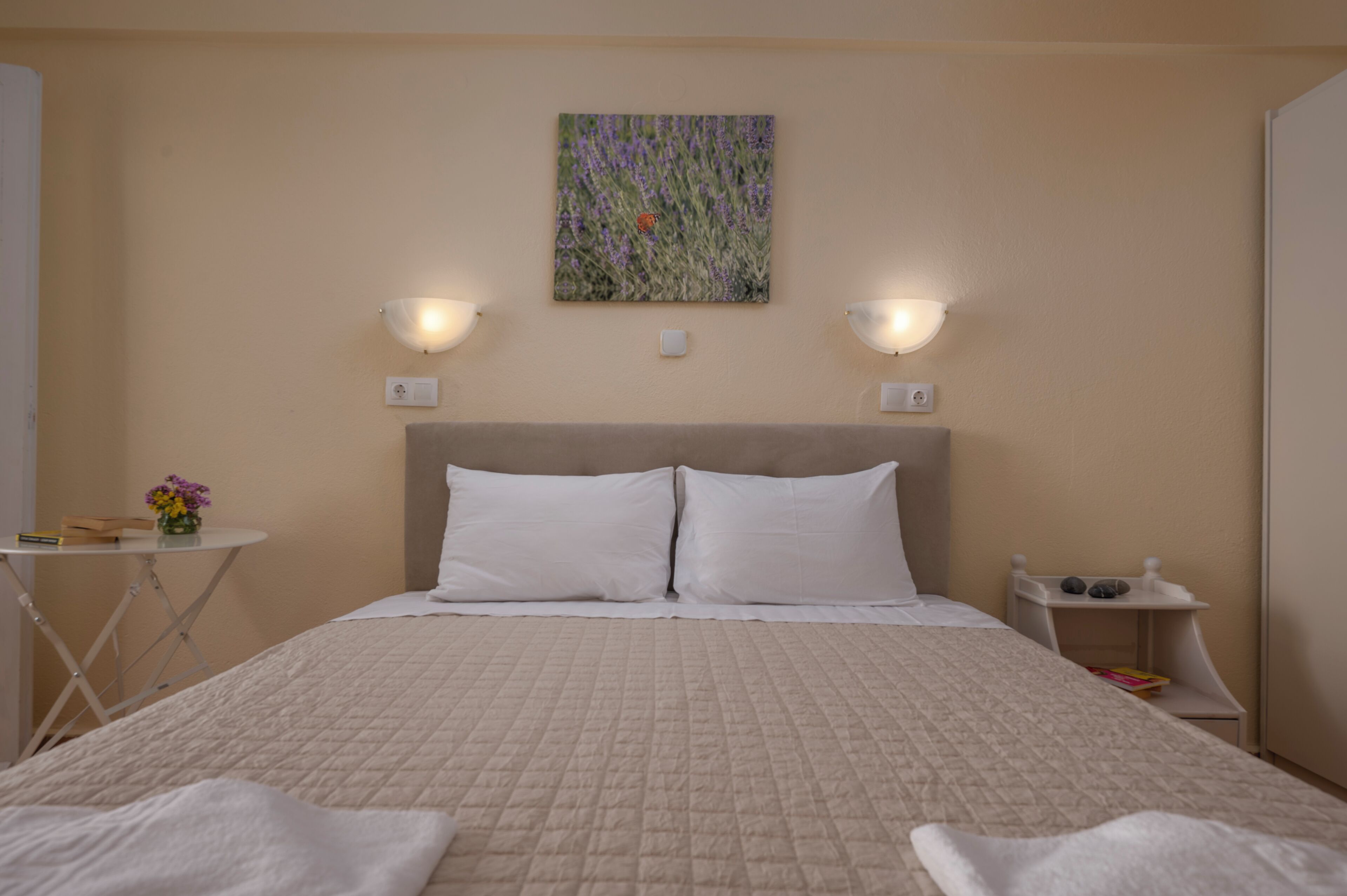 Una cama bien hecha con sábanas blancas, cabecera y dos lámparas de lectura fijadas a la pared.