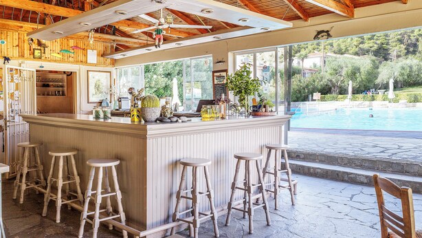 A bar area with stools, a pool view, and a wooden ceiling. - Julia Hotel (Kassandra)