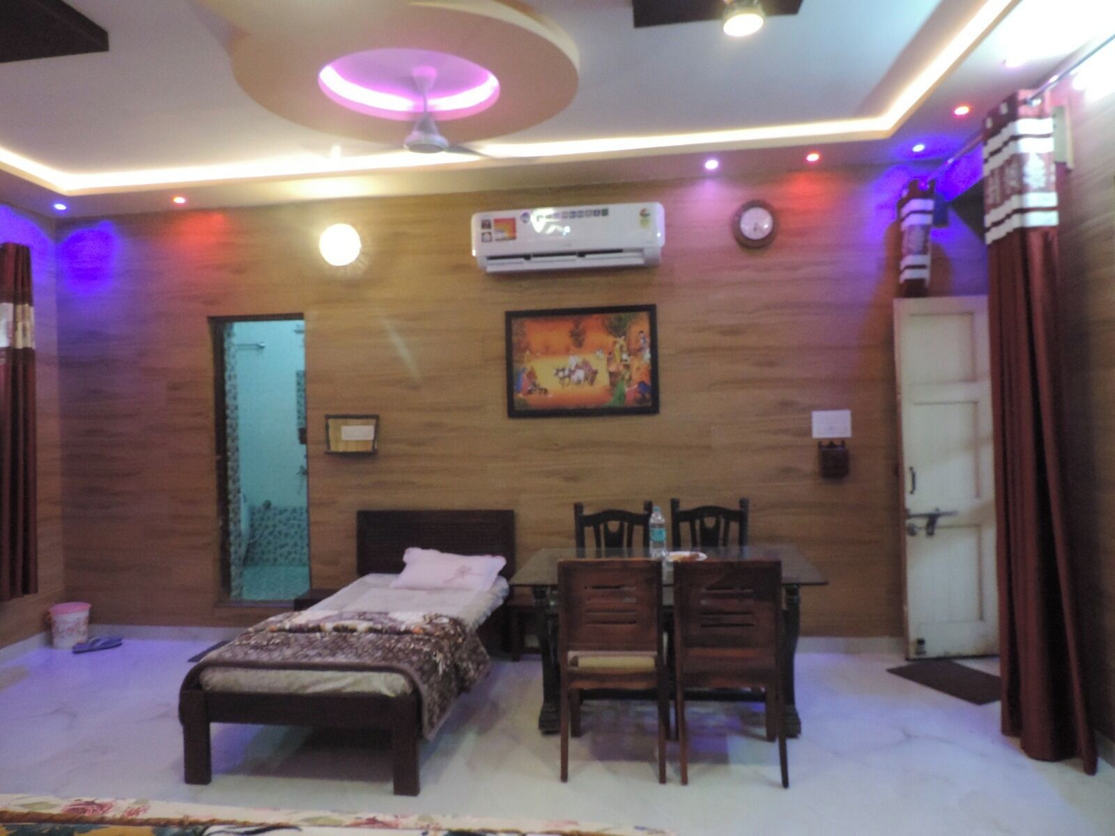 Un dormitorio con cama, una mesa con sillas, un aire acondicionado y un cuadro en la pared.