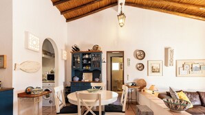 A cozy living room with a round table, white chairs, a brown leather sofa, and a patterned bowl on a side table. - Roseus Villa, Galé, Algarve (Guia)