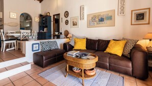 A cozy living room with a brown leather sofa, a wicker coffee table, and a dining area with a white table and chairs. - Roseus Villa, Galé, Algarve (Guia)