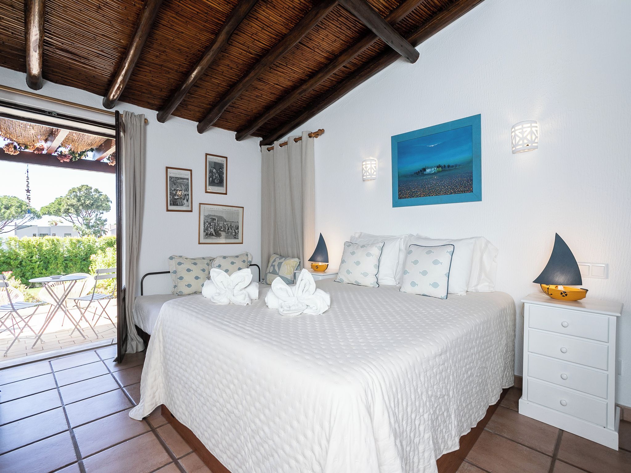 A hotel room with a bed, a nightstand, a painting, and a view of the outdoors.