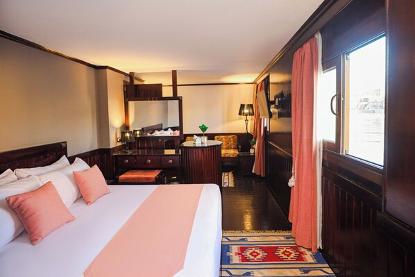 Ein Hotelzimmer mit einem großen Bett, einem Schreibtisch, einem Stuhl, einem Spiegel und einem Fenster mit Vorhängen.