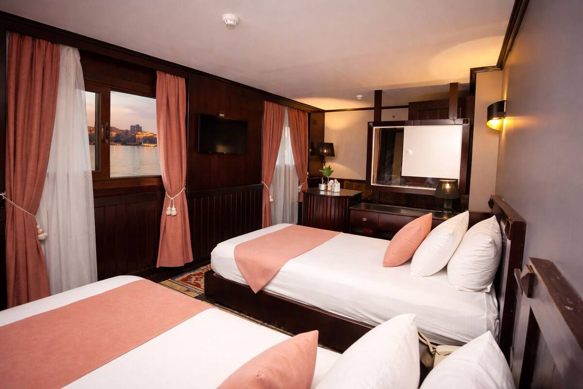 A hotel room with two beds, a desk, a mirror, and a view of a cityscape.
