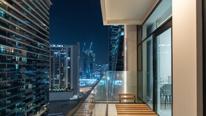 A balcony with a wooden bench, overlooking a cityscape at night. - Bespoke Residences - Urban Oasis  (Dubai)
