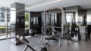 A modern gym with various exercise equipment, large windows, and a view of the city. - Bespoke Residences - Urban Oasis  (Dubai)